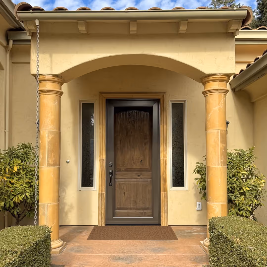 Bronze-brown custom security screen door over a rustic wood entry door